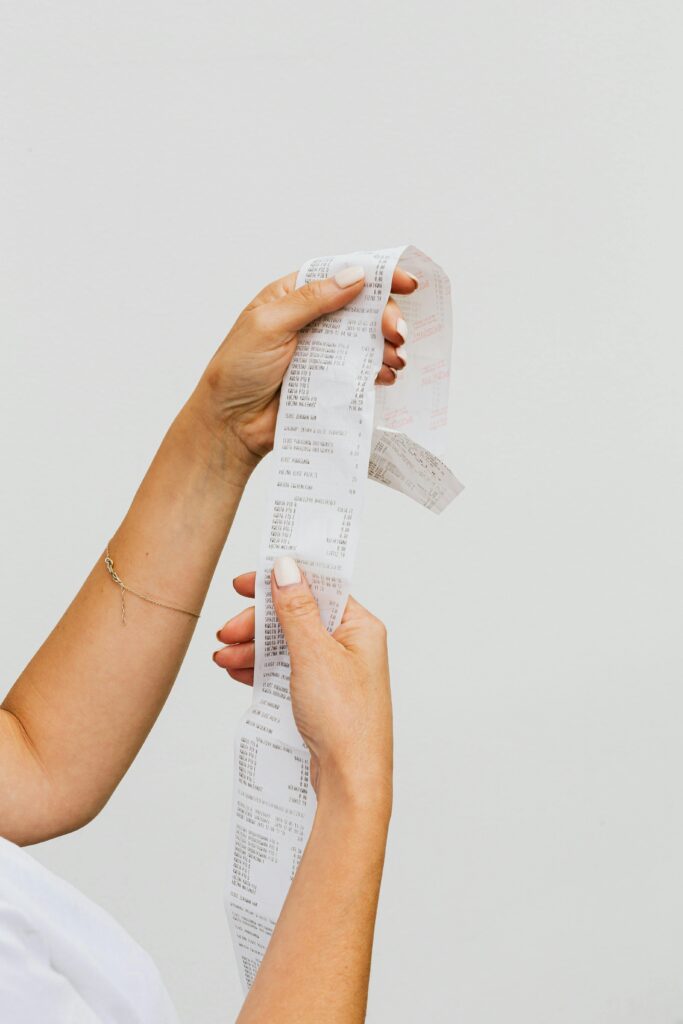 Close-up of woman's hands holding a long receipt against a white background, representing shopping or budgeting.