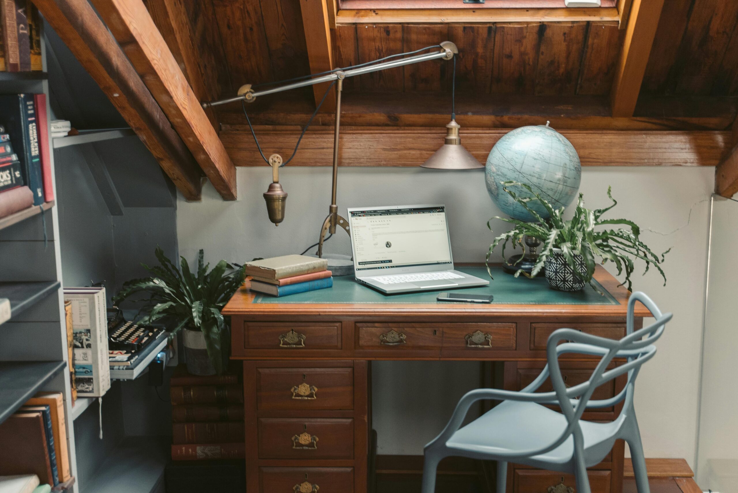 A cozy attic home office featuring a vintage desk, globe, and laptop setup under a skylight.