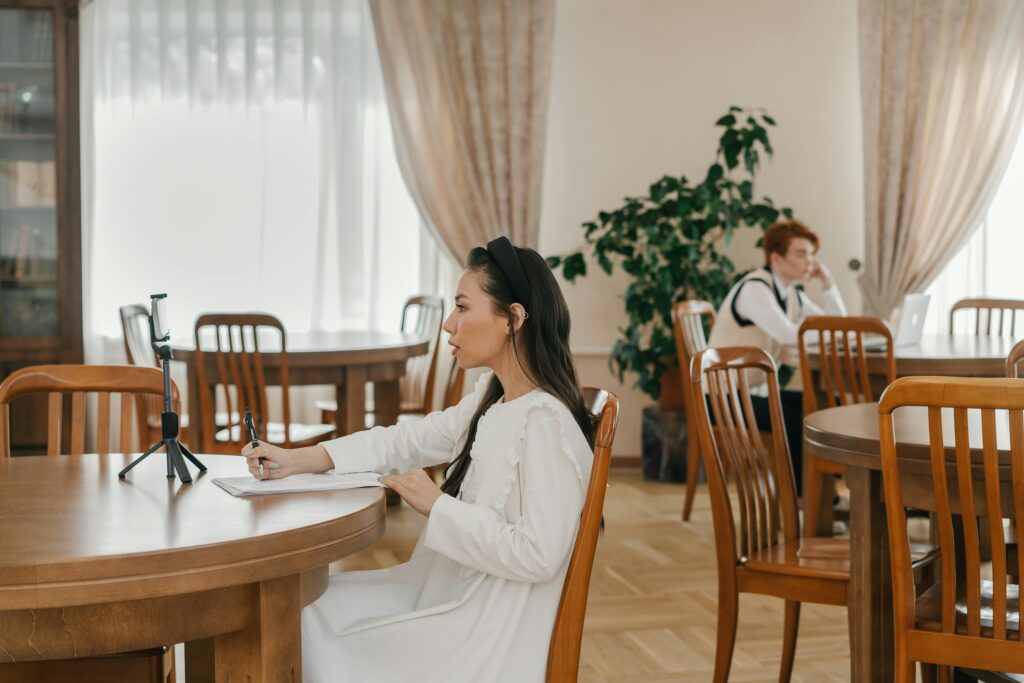 A young woman recording a vlog in a peaceful library with smartphone and tripod.